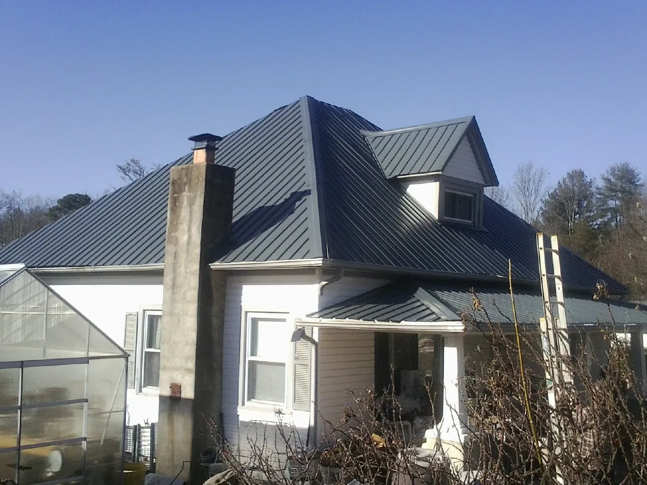 Dark blue standing seam metal roof on a white farmhouse with dormer — Slate & Tile Roof Repair by Roofing Brothers in Hickory Flat