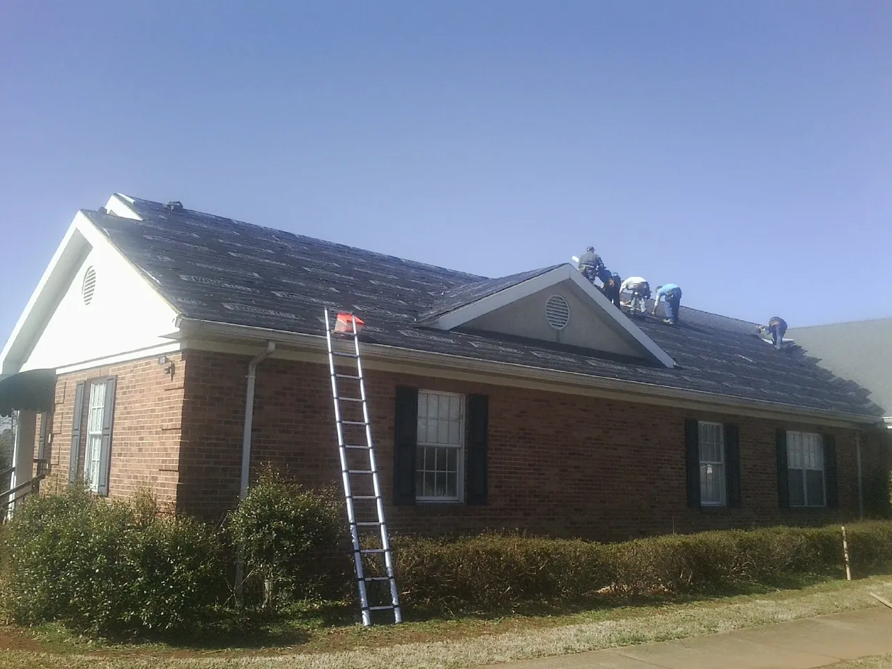 Crew tearing shingles off a brick ranch roof with a ladder set — Metal Roof Repair work by our crew in Hickory Flat
