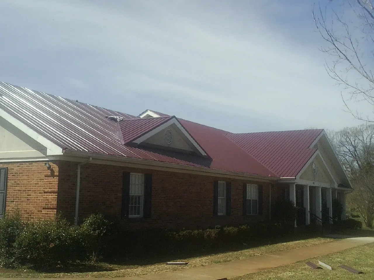 Red metal roof with gabled entries on a long brick building, from a Hail Damage Roof Repair job in Hickory Flat