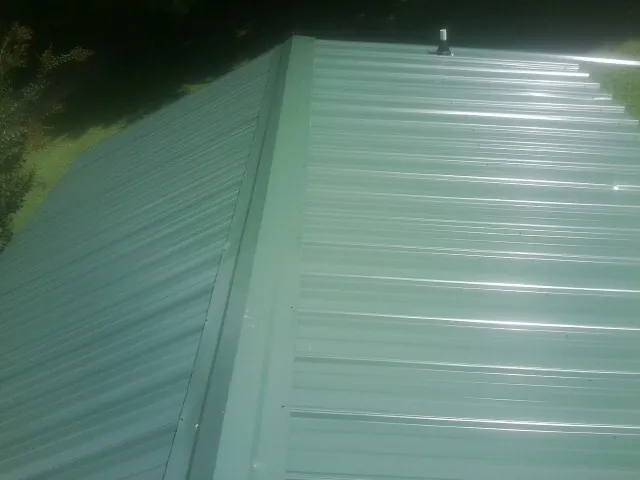 New green metal panels meeting at the ridge of a roof — Flat Roof Repair work by our crew in Hickory Flat