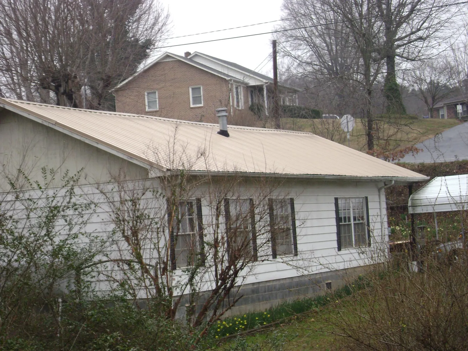 Tan metal roof on a white sided house set into a hillside — Commercial Roofing by Roofing Brothers in Hickory Flat